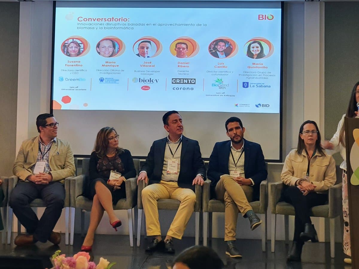 Panel de cinco participantes sentados en un conversatorio, con la pantalla del evento y los logos de las organizaciones al fondo.